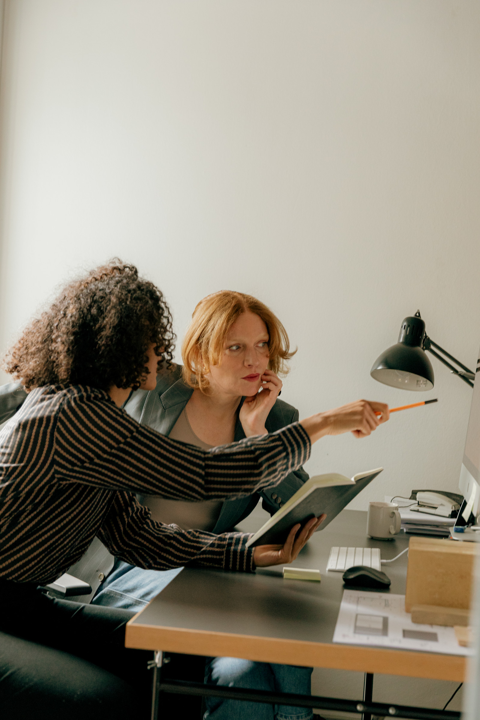 One REALTOR® pointing at a screen, guiding a colleague through her work